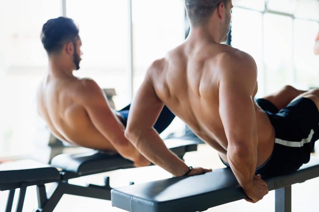 Strong men are doing abs crunches on bench in gym