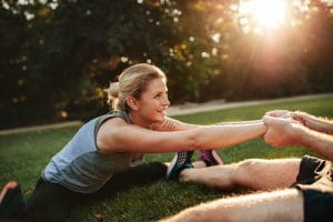 Young health couple exercising in park. Man holding hands of woman and stretching.