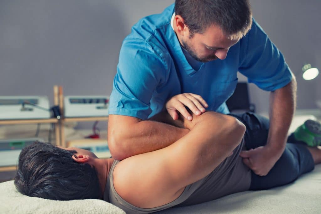Physiotherapist doing healing treatment on man's back. Therapist wearing blue uniform. Osteopathy. Chiropractic adjustment, patient lying on massage table
