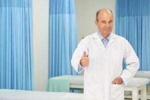 Smiling middle-aged professional chiripractor in labcoat showing thumbs-up